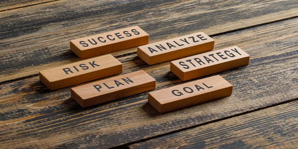 Wooden blocks on a table with business-related words: success, risk, plan, analyze, strategy, and goal.